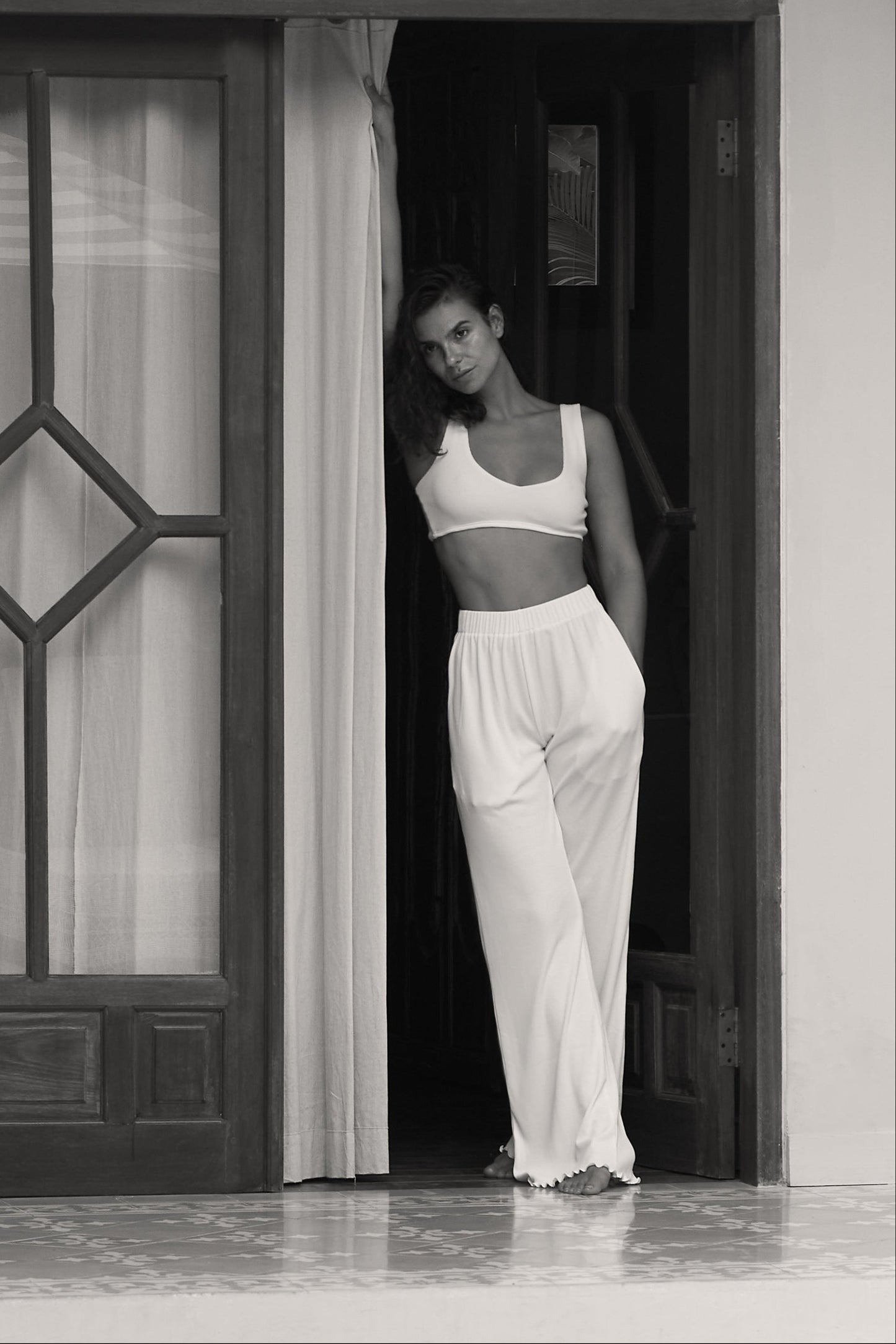 Woman in white ribbed flare pants and top, standing by doorway