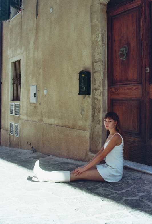 Model wearing white SESE mini dress, sitting outdoors.